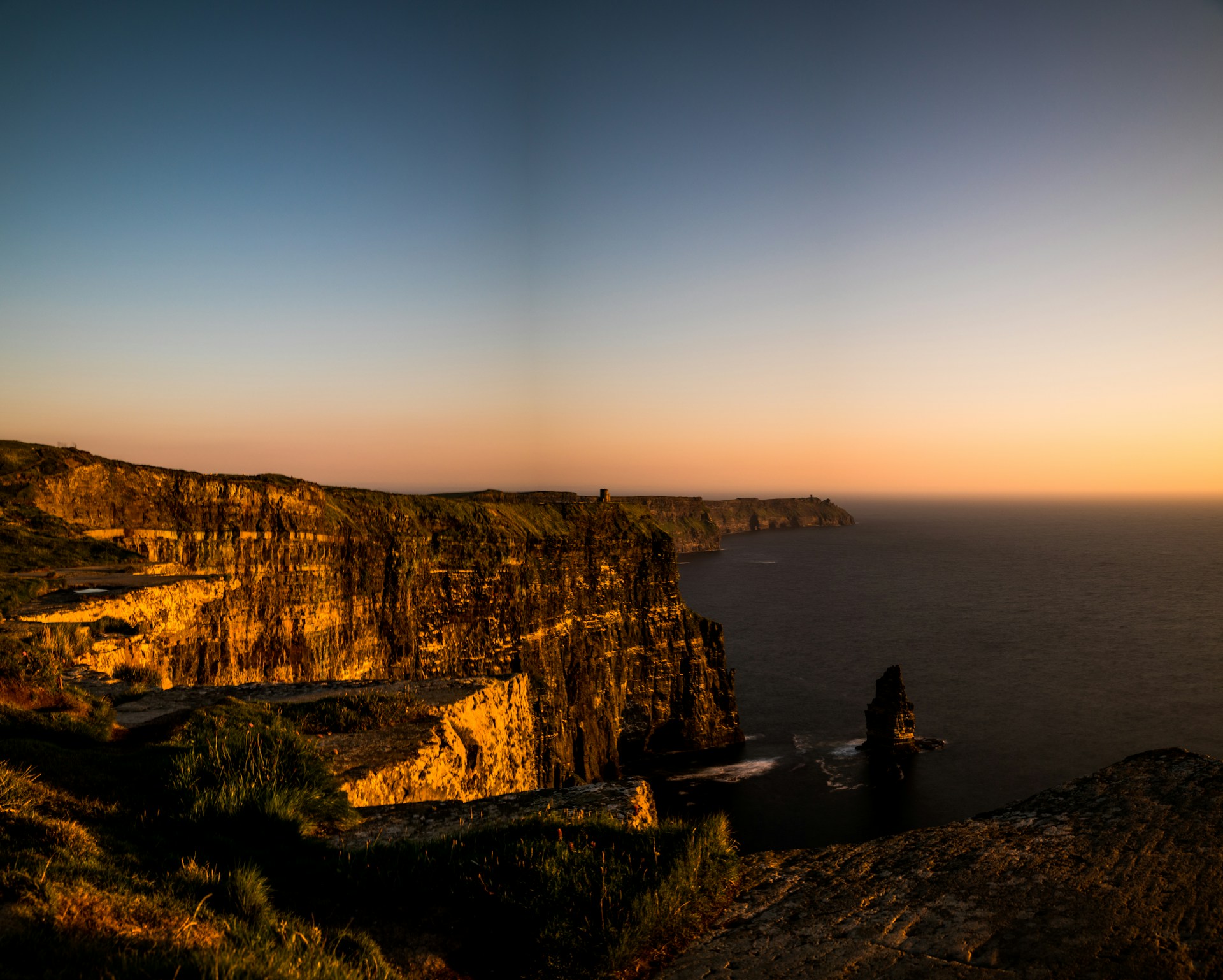 A panoramic view of the dramatic cliffs and turquoise waves at Uluwatu, framed by swaying palm trees under a golden afternoon sky.