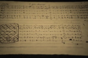 A sheet of music manuscript with printed musical notes and handwritten annotations. The page appears aged, with visible yellowing and ink smudges. A section on the left contains a grid filled with musical notation, while the main body of the page shows lines of musical notes and lyrics.