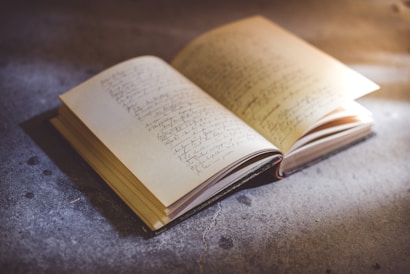 An open notebook with handwritten notes resting on a textured surface. The pages appear yellowed and the writing is slightly faded, suggesting age or frequent use. Light casts a gentle glow on the notebook, creating a warm and inviting atmosphere.