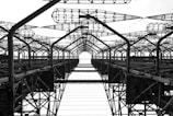 A complex network of metal structures and cables forms an intricate industrial framework. The perspective looks upwards, highlighting the repetitive geometric patterns and intricate lattice work.