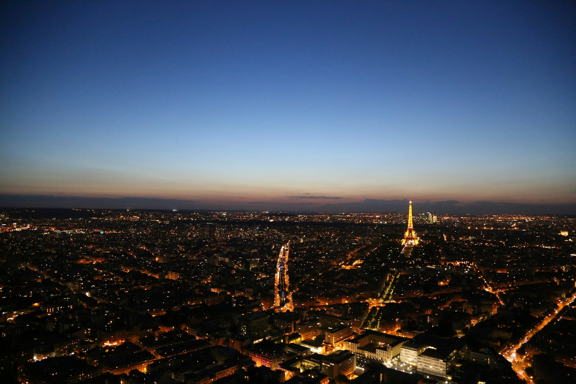 An aerial view of a bustling cityscape at dusk, with twinkling lights and busy streets below.
