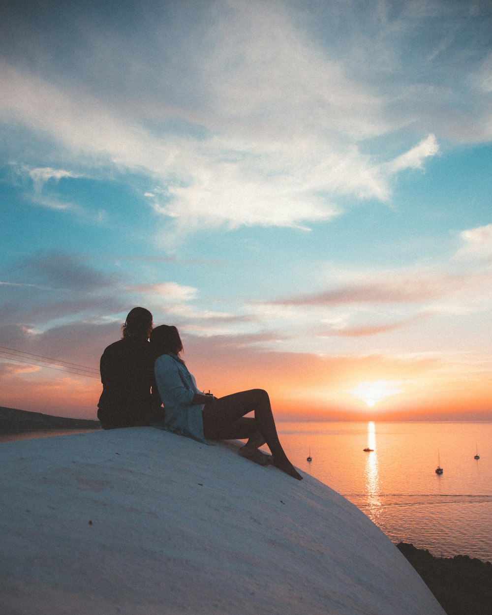 man and woman sitting on white sand during sunset