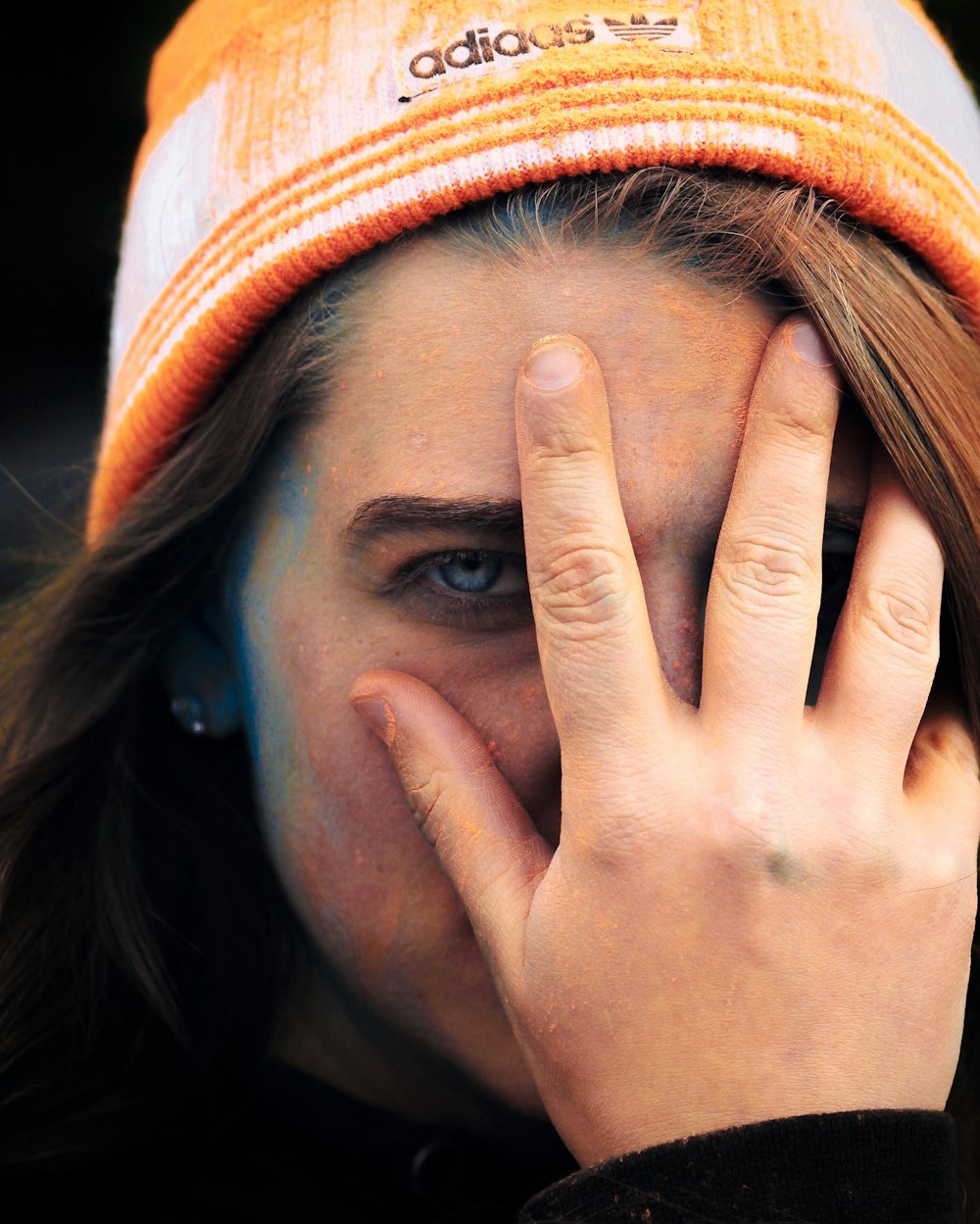 woman wearing adidas cap holding her face
