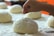 A hand is seen preparing dough with flour sprinkled on top, surrounded by several other pieces of dough resting on a floured surface.