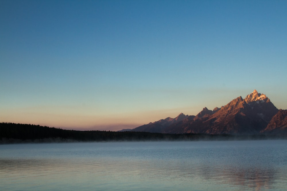 body of water near mountain under blue sky at daytime