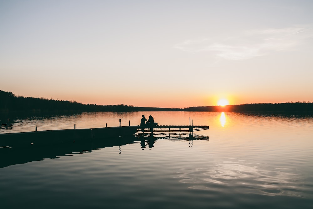 silhouette of two person sitting on dock during golden hour