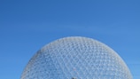 A geodesic dome structure made of interconnected metal bars against a clear blue sky.