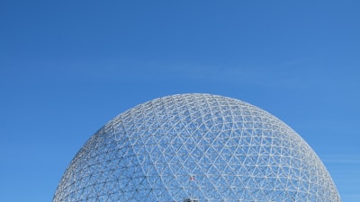 A geodesic dome structure made of interconnected metal bars against a clear blue sky.