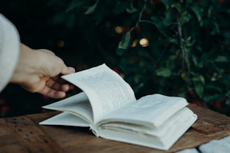 Close-up of hands turning the pages of the book on a wooden table with soft earth-toned decor in the background.