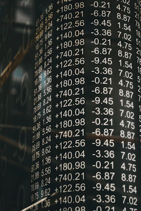 A board displays various financial numbers, including positive and negative values with decimal points. The numbers are aligned in columns, suggesting a stock market or financial data context. The overall scene conveys a sense of an analytic or financial environment.