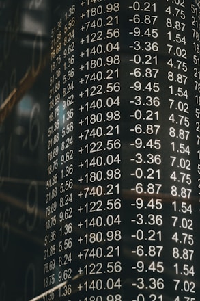A board displays various financial numbers, including positive and negative values with decimal points. The numbers are aligned in columns, suggesting a stock market or financial data context. The overall scene conveys a sense of an analytic or financial environment.