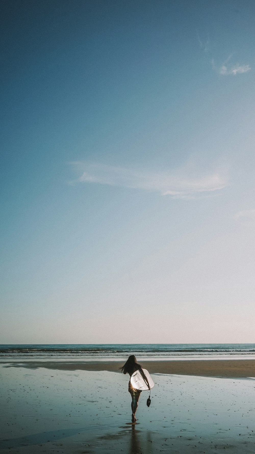 femme tenant une planche de surf blanche marchant sur le rivage