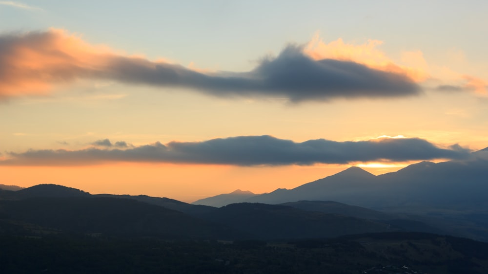 silhouette of mountains under cloudy sky at golden hour