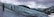A group of people are trekking across a vast, icy glacier with snow-capped mountains in the background under a cloudy sky. They are connected by a rope for safety, wearing snow gear and carrying climbing equipment. The scene conveys a sense of adventure and exploration amid a rugged natural landscape.