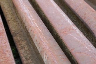 Several rusted metal beams or bars arranged in parallel, showing a reddish-brown coloration due to oxidation. The surface appears rough with visible textures and rust marks.