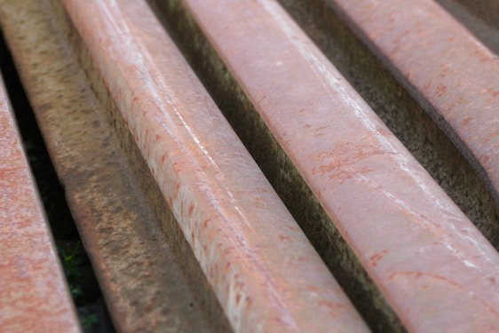 Several rusted metal beams or bars arranged in parallel, showing a reddish-brown coloration due to oxidation. The surface appears rough with visible textures and rust marks.