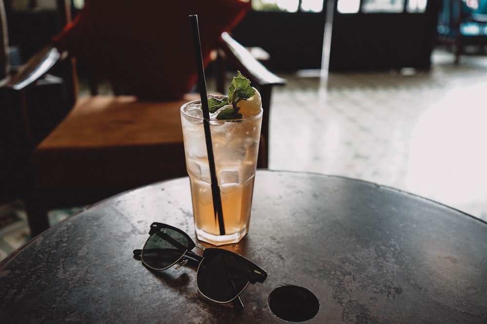 black Clubmaster-style sunglasses beside drinking glass