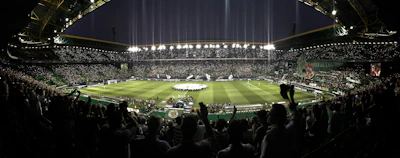 Wide view of a packed stadium at night, illuminated and buzzing with energy.