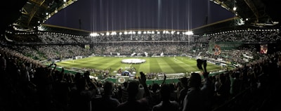 A packed stadium under floodlights with players mid-game chasing the ball.