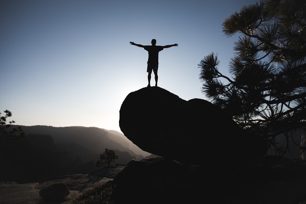 silhouette of man standing on boulder during daytime