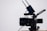 A professional video camera with a large lens and an attached external monitor. Two antennas are mounted on top, likely part of a wireless transmission system. The camera is on a tripod, set against a simple, light-colored background.