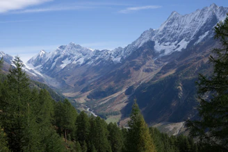 A breathtaking view of the towering northern mountains under a clear blue sky, with greenery and a winding river in the valley below.