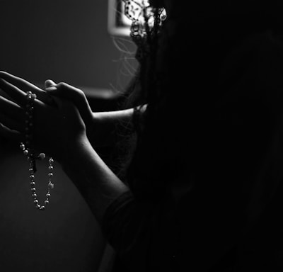 silhouette of woman holding rosary while praying