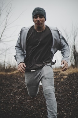 man wearing black shirt and gray jacket with pants while running into plain field