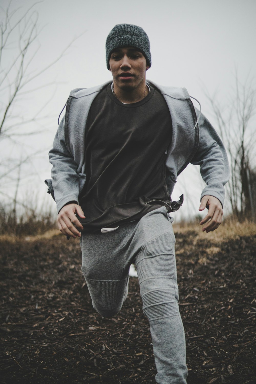 man wearing black shirt and gray jacket with pants while running into plain field