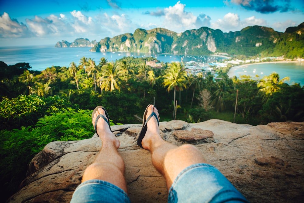 person wearing black flip-flops sitting on rock