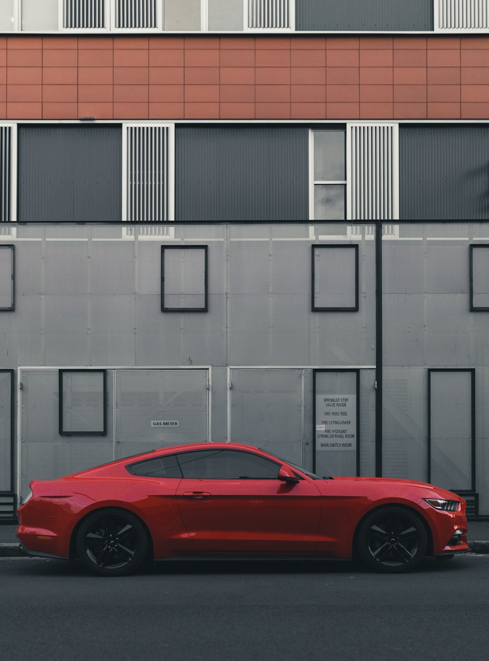 cupé Ford Mustang rojo estacionado al lado del edificio