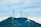 Several wind turbines stand atop a green hill, surrounded by a clear sky filled with clouds. The turbines are evenly spaced and exhibit modern engineering with metal support structures, contributing to a clean energy landscape.