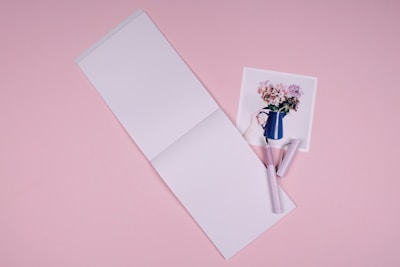 A close-up of a notebook and pen on a pastel pink background, symbolizing mental health journaling.