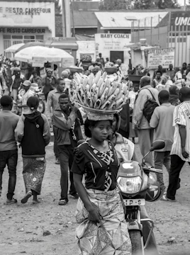 woman carrying bunch of banana on head walking near motorcycle