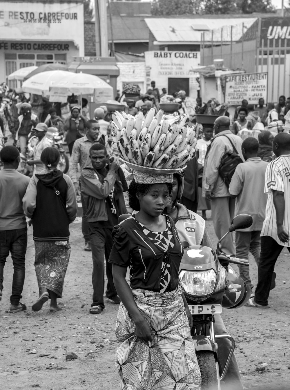 woman carrying bunch of banana on head walking near motorcycle