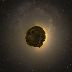 A surreal representation of a small planet effect, where a landscape appears as a sphere in the center of a starry sky. The glow of a distant light casts a halo around the sphere, contributing to a cosmic and otherworldly appearance.