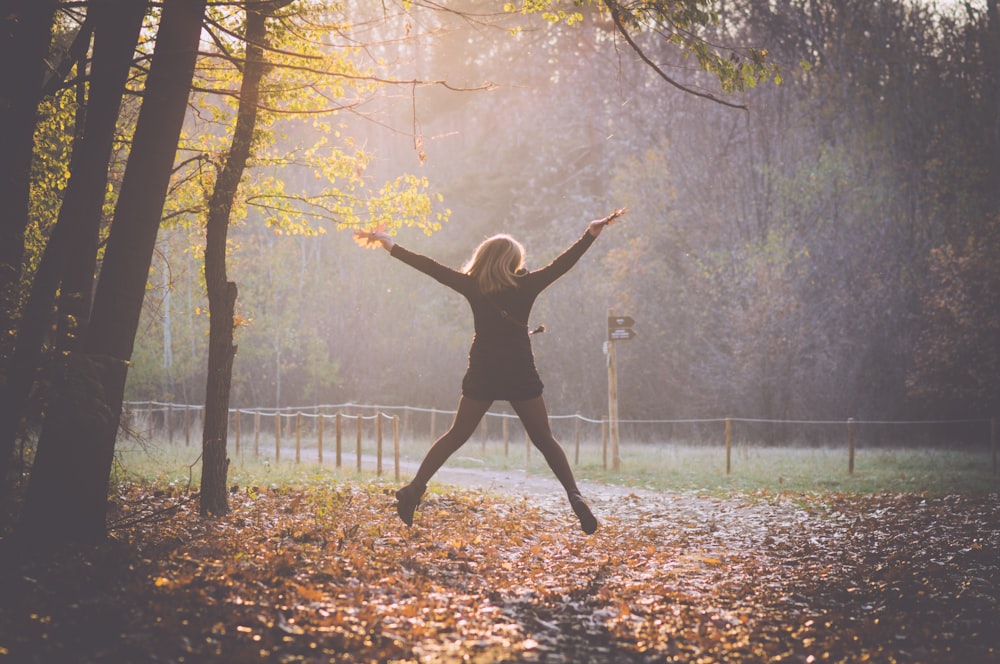 woman jumping under tree surrounded with dried leaves