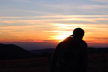 Vibrant sunset behind a mountain silhouette with Caserne sunglasses placed on a backpack.
