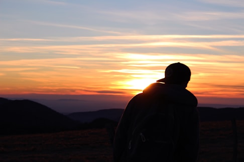 A silhouette of a hiker pausing on a mountain ridge at sunset, with warm orange and purple skies.