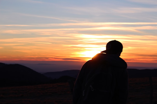 A serene portrait of a traveler silhouetted against a dramatic sunset over rugged mountains