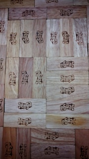 Numerous wooden Jenga blocks are stacked closely together, each block imprinted with the word 'Jenga' in brown lettering. The arrangement forms a seamless wooden surface with varying shades of light brown, creating a pattern of alternating blocks.