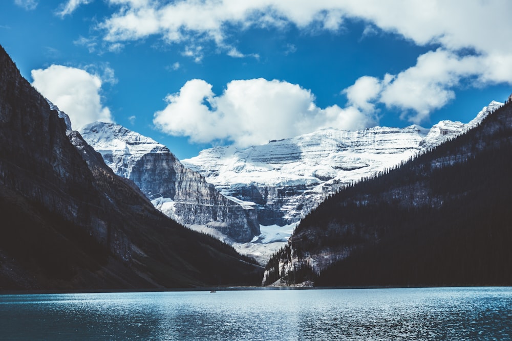 brown and white mountains near body of water under white clouds and blue sky during daytime