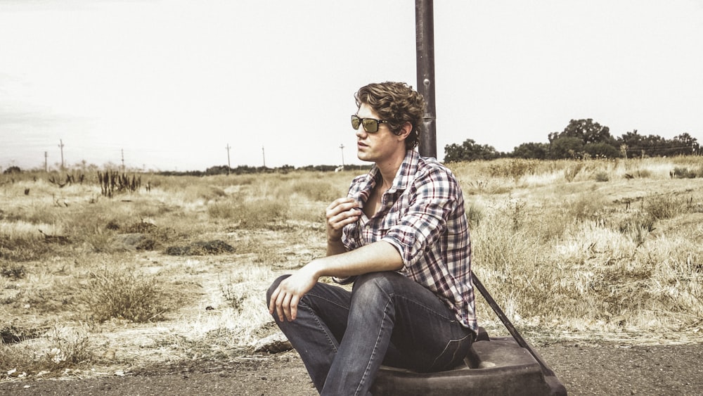 man in white and black plaid sport shirt sitting on tire