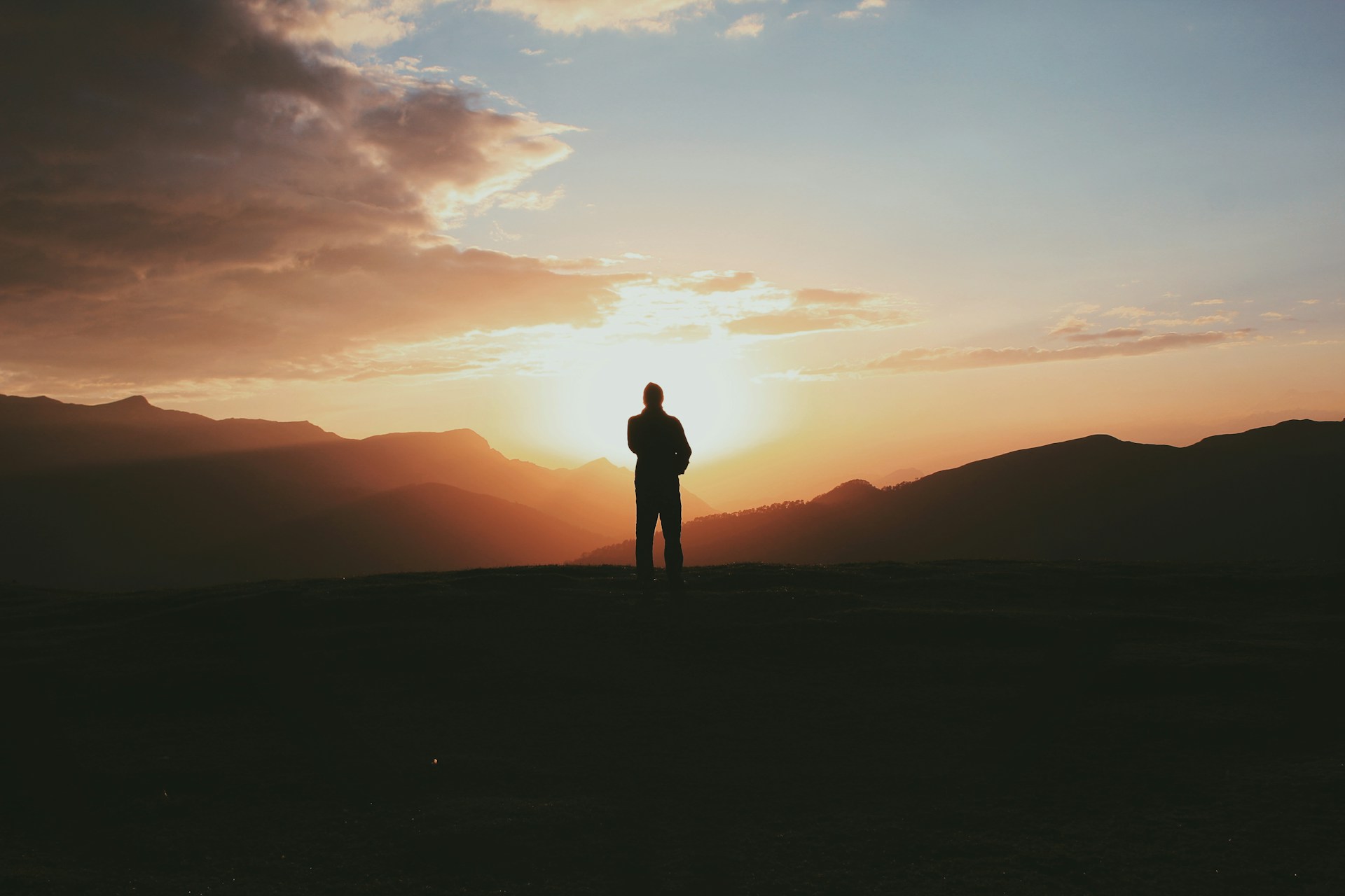 silhouette photo of man standing on mountain during golden hour