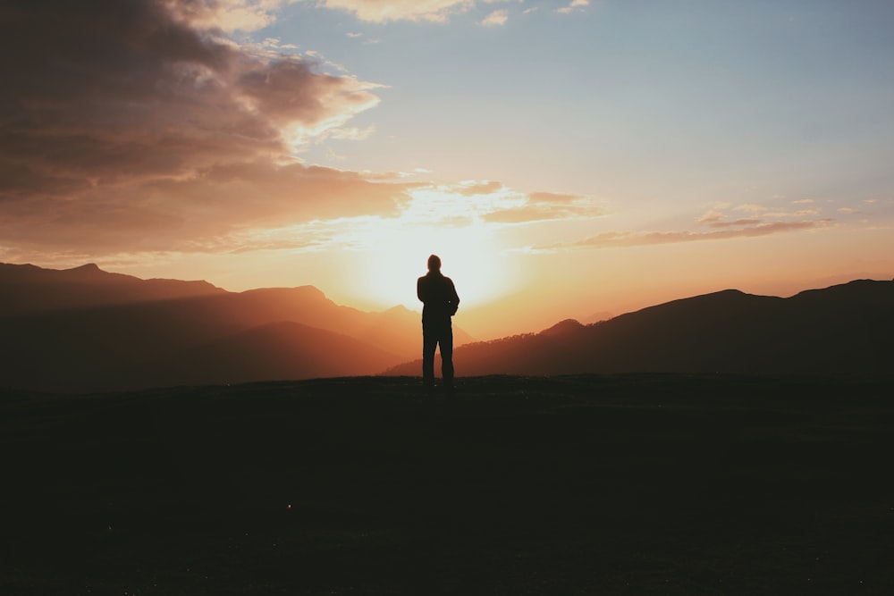 Silhouettenfoto eines Mannes, der während der goldenen Stunde auf dem Berg steht