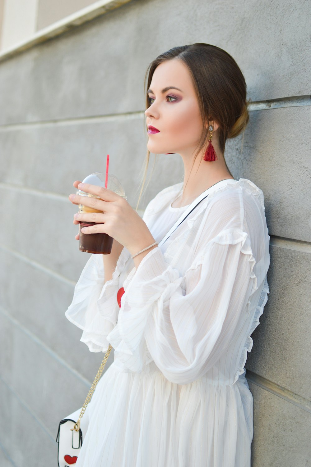 woman leaning on wall holding cups of black beverage