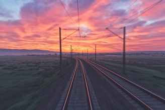 empty train tracks near green grass during sunset