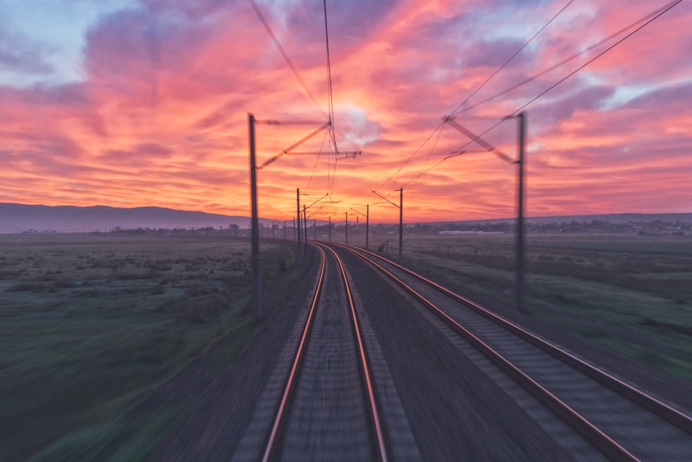 empty train tracks near green grass during sunset