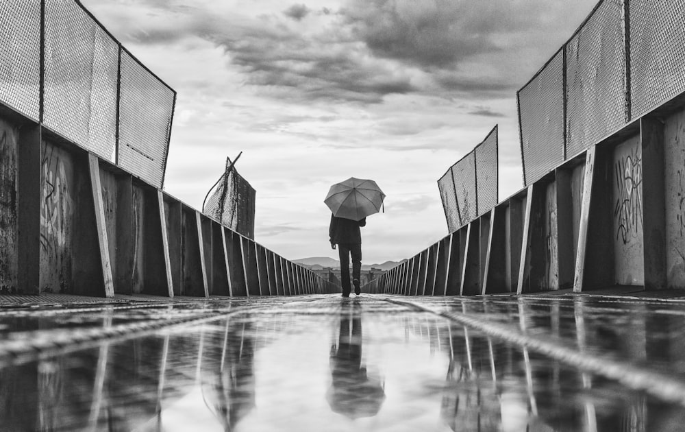 greyscale photo of person standing on pathway while holding umbrella