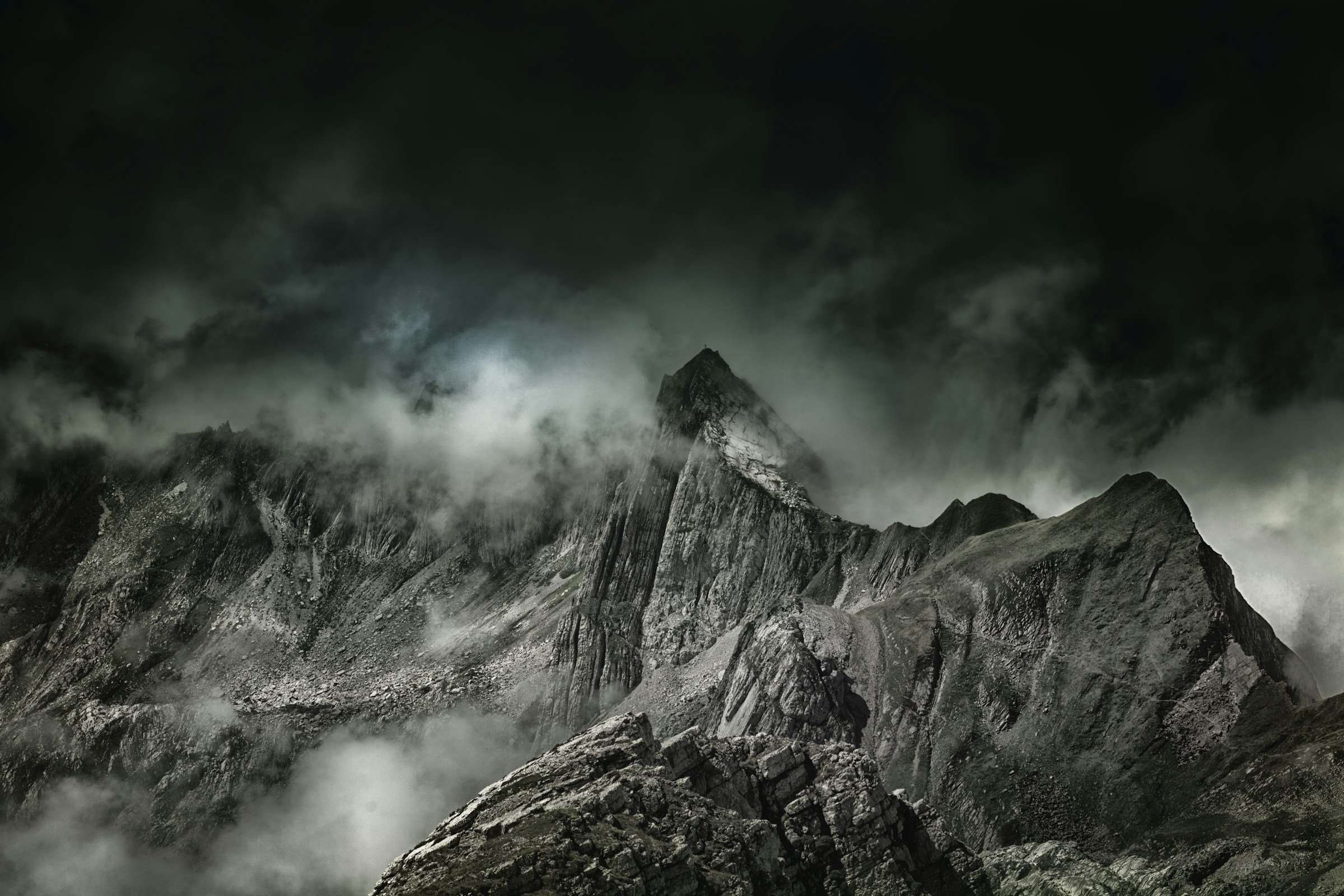 A bare mountain peak under heavy cloud, an hour after sunset.